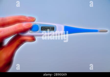 Bei der globalen Kovid-19- oder Corona-Pandemie hält die männliche Hand das klinische Thermometer mit einem Kovid-19-Text auf dem Bildschirm Stockfoto