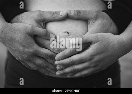Hände zukünftiger Eltern, die den Bauch halten Stockfoto