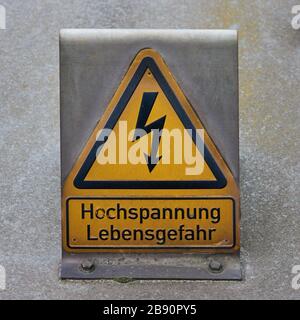 Gelbes Warnschild mit einem stilisierten Blitz und der deutschen Aufschrift: Hochspannung, Lebensgefahr Stockfoto