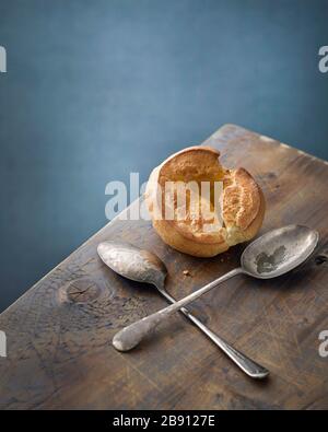 Single Yorkshire Pudding auf einem Holztisch aus Kiefernholz mit zwei verdisten Löffeln Stockfoto