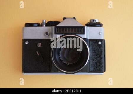 Ansicht von oben auf Vintage-Filmkamera auf gelbem Hintergrund. Schwarzer Metallrahmen aus Silber und Kunststoff mit Linse. Stockfoto