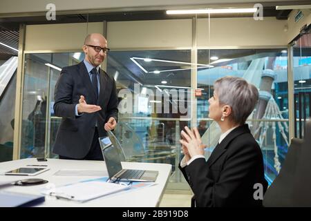 Portrait des lächelnden kahlen Geschäftsmannes, der die weibliche Kollegin im Besprechungsraum grüßt, Kopierer Stockfoto