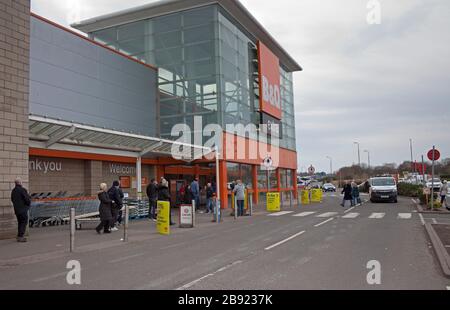 Edinburgh, Schottland, Großbritannien. März 2020. B&Q und Screwfix, Kingfisher UK-Stores, bleiben geöffnet und haben trotz Coronavirus-Pandemie weniger Öffnungszeiten. Die abgebildeten Kunden mussten am Nachmittag am Eingang der Niederlassung des Newcraighall Retail Parks mit einem sehr belebten Parkplatz warten, vielleicht in der Erwartung, dass die Leute gezwungen werden, zu Hause zu bleiben. Die Anzahl der Kunden, die in den Laden dürfen, wurde ebenfalls eingeschränkt Stockfoto