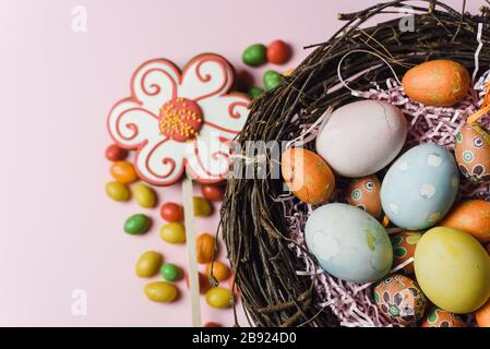 Samara Russland - 03.01.2020: Bemalte und dekorative Eier für den Osterurlaub in einem Zweignest neben Süßigkeiten und Lebkuchen. Osterkarte auf pinkfarbenem Hintergrund. Stockfoto