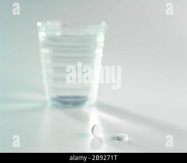 2 Schmerztabletten mit Glas Wasser im Hintergrund auf weiß Stockfoto