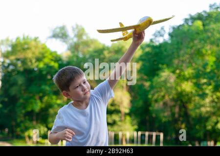 Der junge Junge startet bei Sonnenuntergang mit einem Spielzeuggleiter. Weicher Hintergrund. Stockfoto