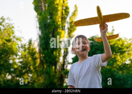 Der junge Junge startet bei Sonnenuntergang mit einem Spielzeuggleiter. Weicher Hintergrund. Stockfoto