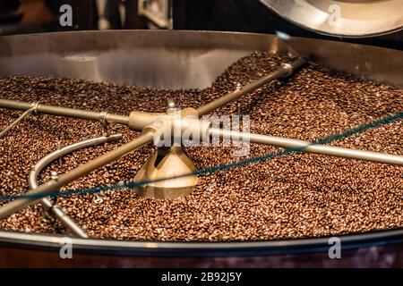 Gebratene Kaffeebohnen, die in der Mischmaschine gemischt werden, Ausrüstung zur Vorbereitung von Bohnen für den weiteren Prozess. Stockfoto