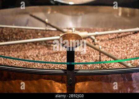 Gebratene Kaffeebohnen, die in der Mischmaschine gemischt werden, Ausrüstung zur Vorbereitung von Bohnen für den weiteren Prozess. Mockup für Logo oder Stempel anmelden. Stockfoto