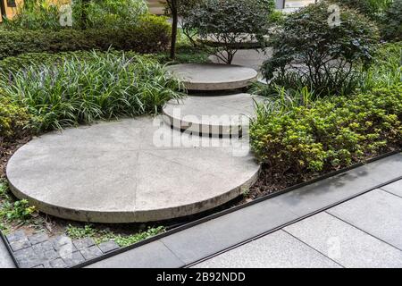 Runde Betonstufen im kleinen Garten. Weg zwischen Büschen und Bäumen. Landschaftsgestaltung nachhaltiger grüner Architektur. Stepping Stones bei GRE Stockfoto