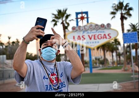 Las Vegas, Nevada, USA. März 2020. Eddie Sarinana aus Las Vegas, der eine schützende Gesichtsmaske trägt, nimmt am 23. März 2020 in Las Vegas, Nevada, ein selfie vor dem Willkommensschild in Las Vegas. Nevada Reg. Steve Sisolak ordnete an, bis zum 16. April unwesentliche Geschäfte im Staat zu schließen, um die Verbreitung des Virus zu bekämpfen. Die Weltgesundheitsorganisation erklärte das Coronavirus (COVID-19) am 11. März zu einer globalen Pandemie. Credit: David Becker/ZUMA Wire/Alamy Live News Stockfoto