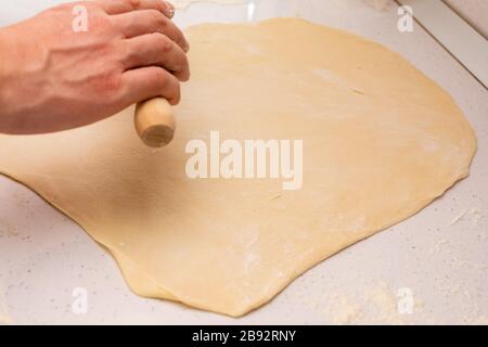 Den Teig ausrollen, den Teig auf einem Holzkitchentisch mit Mehl ausrollen Stockfoto