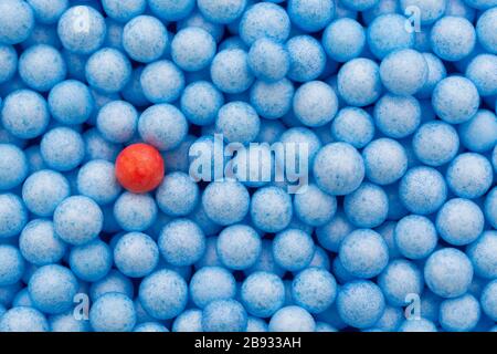 Kleine blaue und rote Polystyrolkugeln farbig. Konzeptionell für Covid-19 Selbstisolation, Krankheitsträger, infizierte Person, isoliert, in der Menge verloren. Stockfoto