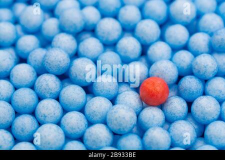 Kleine blaue und rote Polystyrolkugeln farbig. Konzeptionell für Covid-19 Selbstisolation, Krankheitsträger, infizierte Person, isoliert, in der Menge verloren. Stockfoto