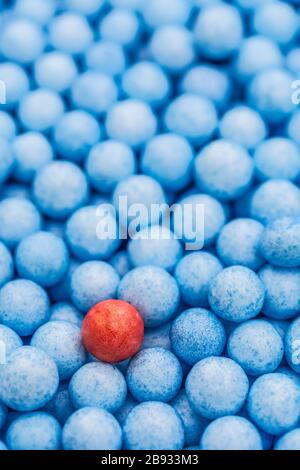 Kleine blaue und rote Polystyrolkugeln farbig. Konzeptionell für Covid-19 Selbstisolation, Krankheitsträger, infizierte Person, isoliert, in der Menge verloren. Stockfoto