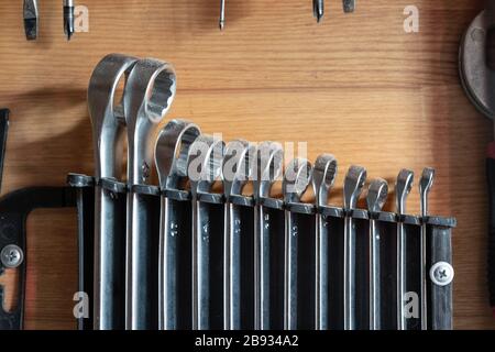 Satz gebrauchter Ringschlüssel aus Metall, der in Kunststoffhalter gegen die Holzwand montiert und gehängt ist. Werkstattschlüssel Werkzeuge und Geräte Industrie Stockfoto