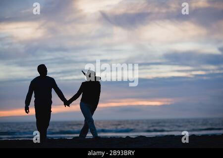 Mitte nach paar Hände halten und entlang einem abgelegenen Strand bei Sonnenuntergang. Stockfoto