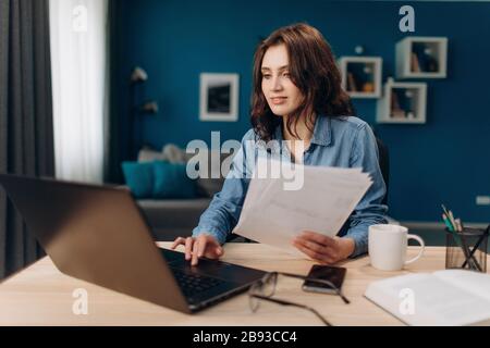 Selbstbewusste Dame, die an einem Laptop arbeitet und Dokumente liest Stockfoto
