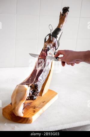 Schneiden Sie die Scheiben von Jamon Iberico in der Küche auf Holzständer gegen die weiß geflieste Wand Stockfoto