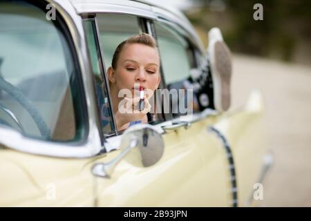 Frau sitzt im Auto und Anwendung Lippenstift Stockfoto