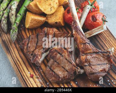 Gegrillte Lammkoteletts auf einem Holzbrett mit Spargel, roter Soße, Kartoffeln Stockfoto