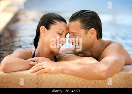 Fröhliches Paar im mittleren Erwachsenenalter lächelt, während es in der Nähe eines Schwimmbades steht. Stockfoto