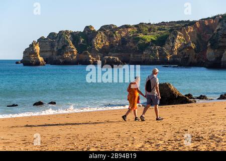 Lagos, Portugal - 7. März 2020: Älteres Paar, das bei Sonnenuntergang am Strand spazieren geht Stockfoto