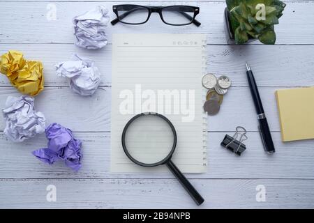 Bunte zerknitterte Papierkugel, Stift und Lupe auf dem Tisch Stockfoto