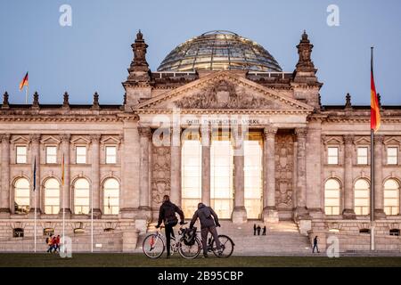 23. März 2020, Berlin: Zwei Radfahrer kommen vor dem Reichstags-Gebäude, dem Sitz des Deutschen Bundestages, auf ihre Räder. Der Bundestag will sich trotz der Koronakrise am Mittwoch zu einer Sitzung treffen. Um die Ausbreitung des Corona-Virus zu verlangsamen, hat die Bundesregierung das öffentliche Leben erheblich eingeschränkt. Foto: Carsten Koall / dpa Stockfoto