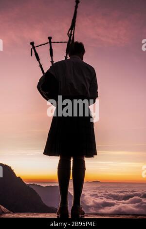 Silhouette eines schottischen Mannes in Kilt, der bei Sonnenaufgang Dudelsack am Mount Bromo in Indonesien spielt. Es war eine spektakuläre Szene mit der Ambient-Musik. Stockfoto