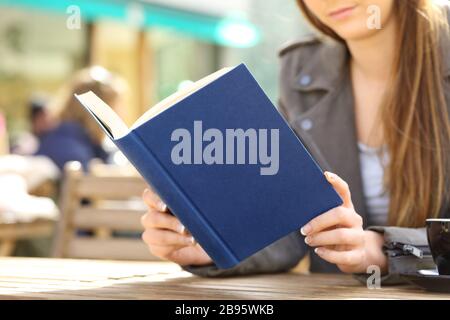 Nahaufnahme der jungen Frau liest ein hartes blaues Buch auf einer Café-Terrasse Stockfoto