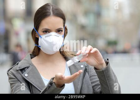 Porträt einer ernsthaften Frau mit Schutzmaske mit Händededesinfektionsmittel und Blick auf die Kamera auf der Straße Stockfoto