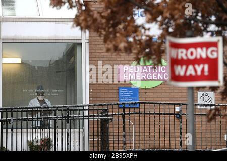 New York City, USA. März 2020. Eine Krankenpflegerin hört auf, ihr Smartphone im Elmhurst Hospital Center zu sehen, während die Menschen im Regen stehen, um auf die Coronavirus Krankheit (COVID-19) im New Yorker Stadtbezirk Queens, New York, am 23. März 2020 getestet zu werden. Leute, die in der Warteschlange warteten, berichteten, bis zu vier Stunden zu warten; reg. Andrew Cuomo hat berichtet, dass es im Staat New York mehr als 20.000 positive Coronavirus Fälle gibt, in New York City mehr als 12.000 (fünf Boroughs). (Anthony Behar/Sipa USA) Credit: SIPA USA/Alamy Live News Stockfoto