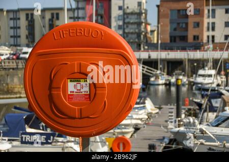 SWANSEA, WALES - JULI 2018: Lebensrettender Gürtel in einem leuchtend orangefarbenen Gehäuse an der Seite des Yachthafens von Swansea Stockfoto