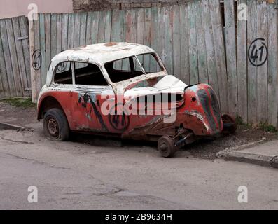 Defektes Oldtimer auf schmutziger Fahrbahn in der Nähe des alten Holzzauns Stockfoto