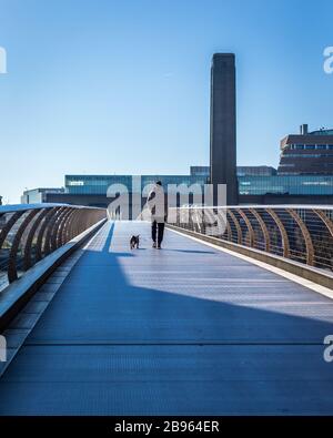 London, England - 23. März 2020: Ein einsamer Wanderer und Hund auf der Millenniumsbrücke im desertierten London unter Sperrstelle während des Corona-Virus-Covid19-Ausbruchs. Stockfoto