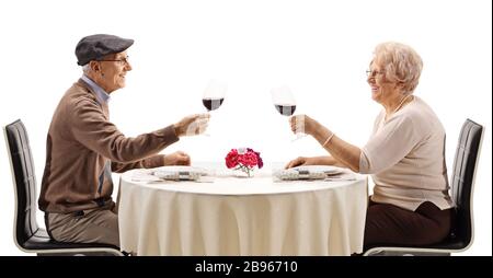 Älteres Paar, das Jubele mit Rotwein an einem Tisch macht, der auf weißem Hintergrund isoliert ist Stockfoto