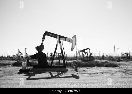 Schwarz-Weiß-Ölpumpen arbeiten in der sonnigen kalifornischen Wüste. Diese Wagenheber können bei jedem Hub 5 bis 40 Liter Rohöl und Wasseremulsion extrahieren. Stockfoto