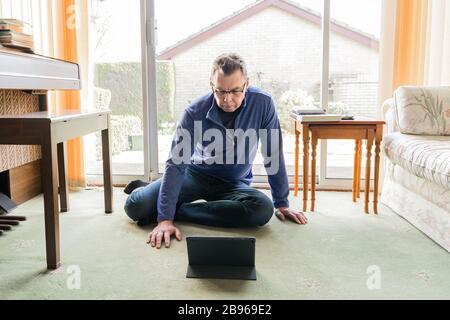 50 etwas männlich in Coronavirus Selbstisolierung zu Hause, sitzend vor dem Fenster im Wohnzimmer, mit Blick auf Tablet-Computer-Pad Stockfoto