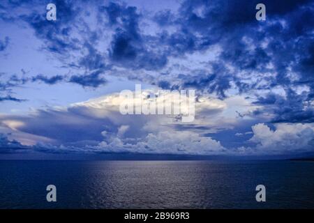 Einzigartige Körper von cumulus Gewitterwolken über dem Horizont des Ozeanwassers zeichnen sich im Hintergrund des blauen Himmels ab. Klimakonzept Umwelt Stockfoto