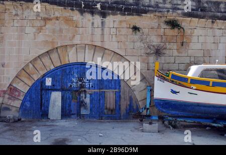 Ein traditionelles Fischerboot befindet sich auf einem Anhänger in der Nähe einer alten Anlage für Marine-Propst an der Küste in Cospicua, Malta, einer der drei Städte. Stockfoto