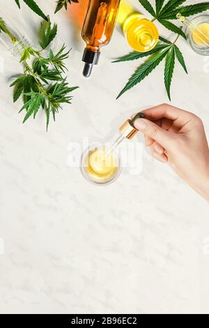 Pipette mit kosmetischem CBD-Öl in weiblichen Händen mit verschiedenen Flaschen mit Cannabisöl und Hanfblättern, Marihuana Stockfoto