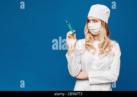 Hübscher weiblicher Arzt mit weißer medizinischer Robe, die Spritze auf blauem Hintergrund hält, isoliert mit Kopierraum. Konzept für das Gesundheitswesen und die Pharmakologie Stockfoto