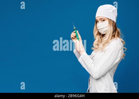 Hübscher weiblicher Arzt, der eine weiße medizinische Robe trägt und die Spritze am blauen Hintergrund hält, kopiere Platz für deinen Text. Gesundheitswesen und Pharmakologie Stockfoto