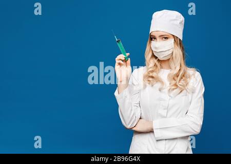 Schöne junge Krankenschwester in medizinischer Robe mit Spritze, isoliert über blauem Hintergrund mit Kopierraum. Medizinische Injektion. Ziemlich junge Frau Doktor Stockfoto