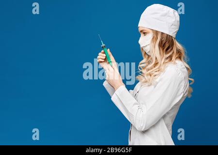 Schöne junge Krankenschwester in medizinischer Robe mit Spritze, isoliert über blauem Hintergrund mit Kopierraum. Medizinische Injektion. Ziemlich junge Frau Doktor Stockfoto