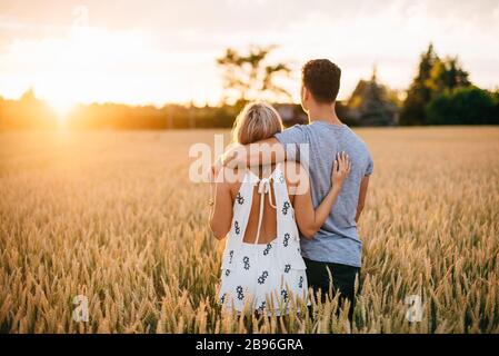 Rückansicht des jungen Paares, das in goldenem Weizenfeld steht und umarmt. Stockfoto