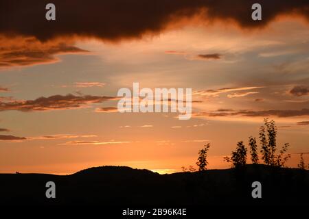 Dramatische dunkelorangefarbene Wolken in einem Sonnenuntergang über fernen Hügeln in Großbritannien Stockfoto