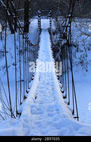 Hängende Fußgängerbrücke über den Fluss im Winterwald Stockfoto