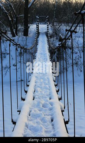 Landschaft mit Fußgängerbrücke über den Fluss im Winterwald Stockfoto